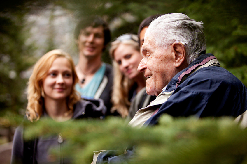 Elderly gentleman surrounded by young men and women.